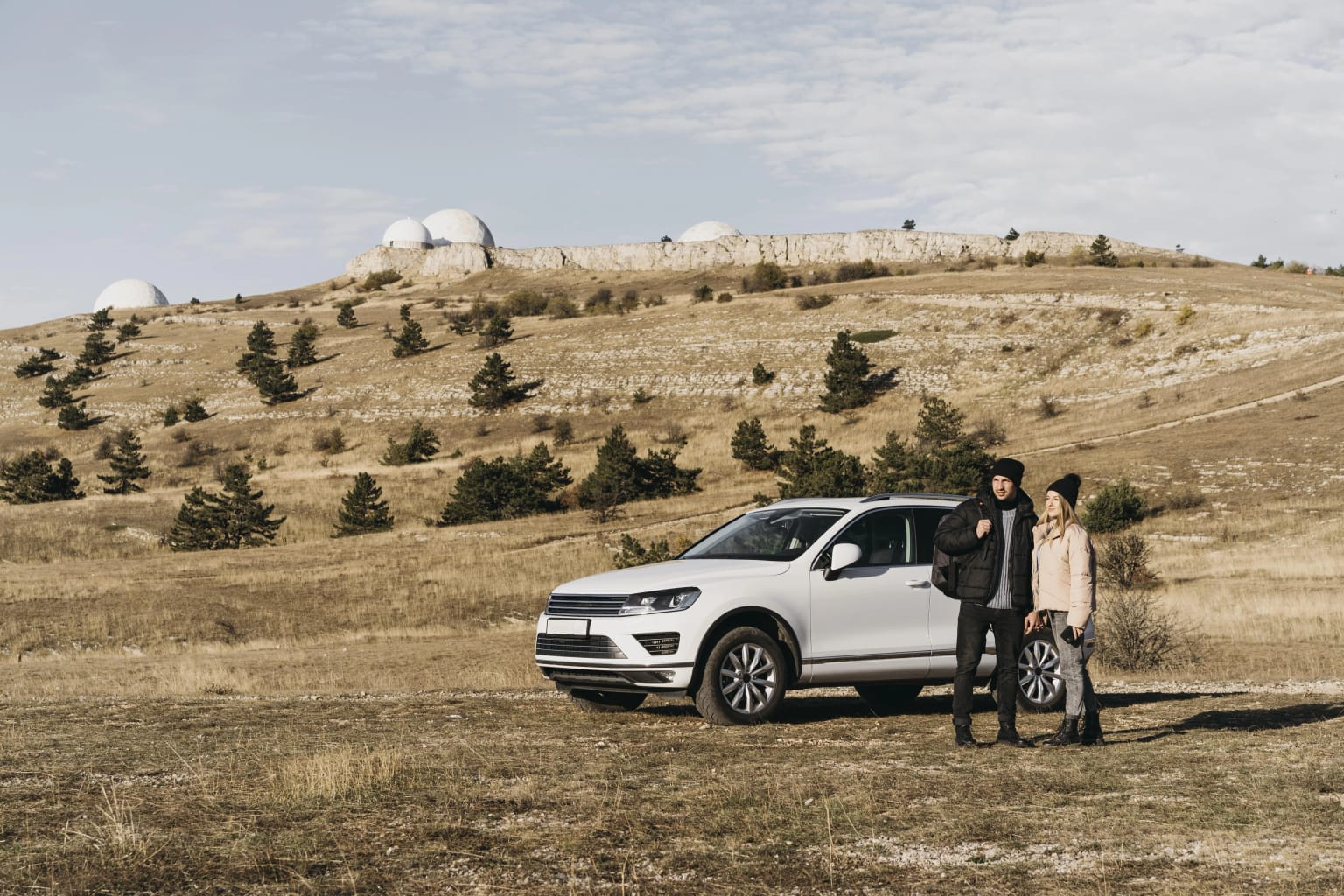 Two people standing beside a white SUV on an open hillside